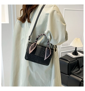 Detail of a black textured crossbody bag with silk scarf handle on a beige trench coat