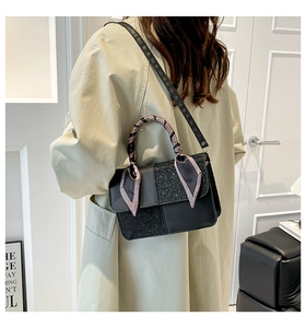 Detail of black crossbody bag featuring a glitter flap and silk scarf handle decoration
