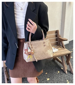 Dettaglio della borsa in pelle scamosciata taupe con manici marroni e ciondolo orsetto