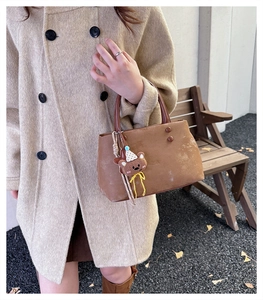 Borsa tote in pelle scamosciata marrone con ciondolo a orsetto su panca in legno autunnale