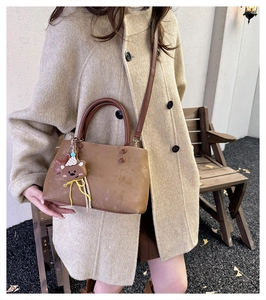 Dettaglio di borsa a secchiello marrone con ciondolo a orsetto e texture opaca su cappotto