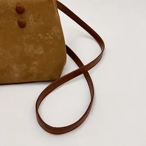 Dettaglio borsa a secchiello in camoscio marrone con fibbie in resina e tracolla sottile