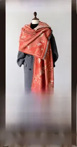 Detail eines rot-weißen Kaschmir-Schals mit Ahornblatt-Muster und Fransen am grauen Mantel