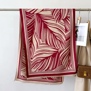 Detail of red and white leaf print scarf with tassels styled on a beige trench coat