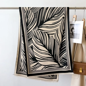 Elegant black and white palm leaf print scarf with tassels hanging on a hanger