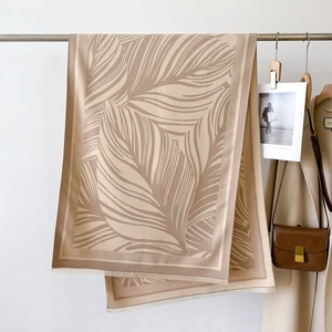 Detail of beige and brown leaf pattern scarf with fine tassels on a metal hanger
