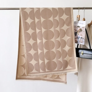 Close-up of geometric knit scarf with beige circles and tassels on a metal rack