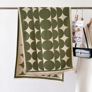 Close-up of a thick geometric knit shawl with tassels in dark green and beige tones