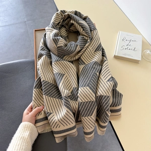 Detail shot of chunky knit scarf showing beige and grey geometric patterns and soft fringes