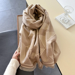 Close-up of a beige and brown geometric knit scarf with fringe on a cozy table setting