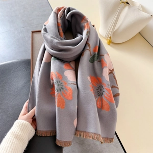 Elegant grey scarf with vibrant orange floral print and tassels on a wooden tray