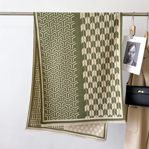 Close-up of geometric knit scarf with green and beige Y-pattern and soft fringe texture