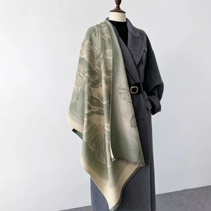Detail of green floral knit scarf with fringe edge on a mannequin with coat