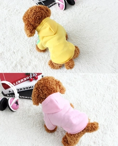 Close-up of yellow and pink fleece pet hoodies on soft plush rug with cozy lifestyle props