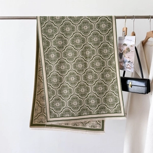 Détail d'une écharpe en maille vert olive avec motifs floraux et franges délicates