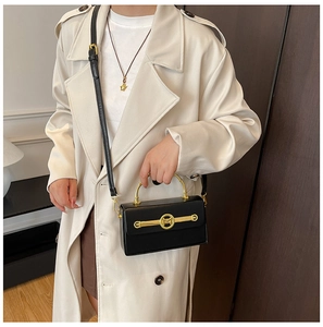 Detail der schwarzen Kunstlederhandtasche mit goldenem M-Logo und rundem Metallgriff