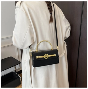 Detail der schwarzen Box-Tasche mit M-Logo Goldbeschlägen und Bambusgriff auf beigem Trenchcoat