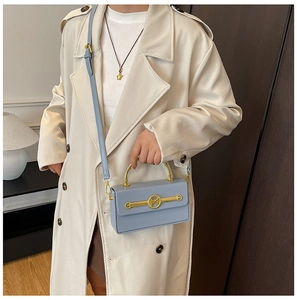 Details der hellblauen Box-Handtasche mit goldnem Griff und Verschluss am Trenchcoat