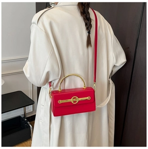 Detailansicht einer roten Handtasche mit goldenem M-Logo und gebogenem Metallgriff