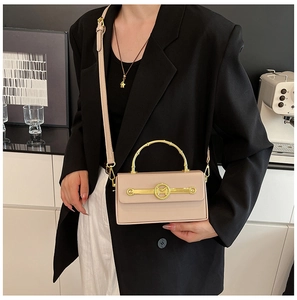 Detail einer beigen Lederbox-Tasche mit goldenem Bogengriff und M-Logo am Model