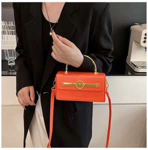 Detail der orangen Lederbox-Tasche mit goldenem M-Griff, getragen von einem Modell in Schwarz
