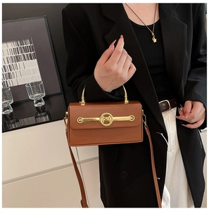 Nahaufnahme der braunen Lederhandtasche mit goldenen M-Beschlägen und schwarzem Anzug