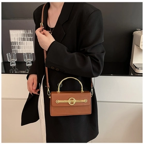 Braune Lederbox-Tasche mit goldenem M-Logo und Metallgriff im Bambus-Stil am Modell