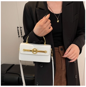 Weiße glänzende Box-Tasche mit goldenem M-Logo und Metallgriff auf schwarzem Anzug