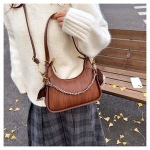 Detail of brown crescent bag with woven texture and decorative silk scarf on chain strap