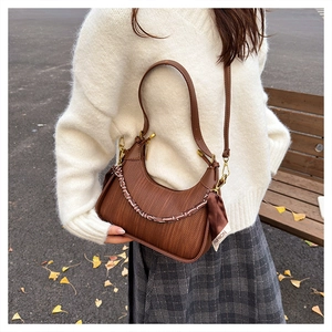 Close-up of brown half-moon bag with woven texture, silk scarf and decorative chain