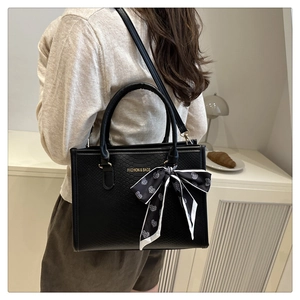 Détail du sac à main noir à texture animale avec foulard en soie et logo doré