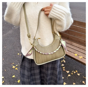 Detail of grey-green woven crescent bag with decorative silk scarf in outdoor setting