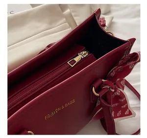 Détail du sac cabas bordeaux avec fermeture éclair dorée et poignée ornée d'un foulard