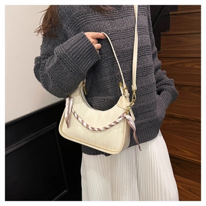 Close-up of beige woven crescent bag featuring a decorative striped silk scarf and gold chain