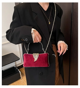 Close-up of red velvet evening bag with gold leaf clasp and chain strap on black blazer