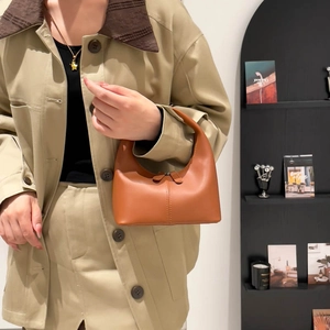 Minimalist orange leather hobo bucket bag held by a model in a warm lifestyle setting
