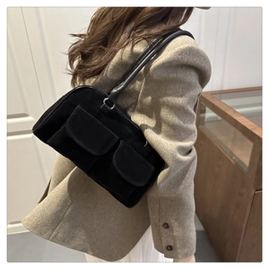 Side view of black matte suede shoulder bag with dual flap pockets worn with grey blazer