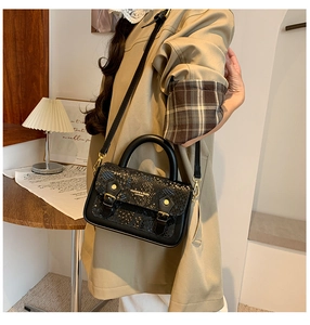 Detail of black crossbody bag with snake print flap and gold hardware on trench coat