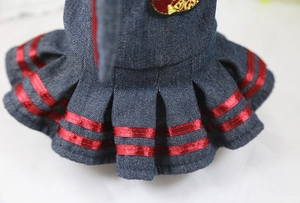 Detail of denim pleated pet skirt featuring parallel red ribbons and a woven patch
