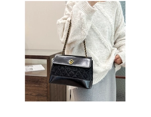 Detail of elegant black quilted crossbody bag with gold chain strap and rotary lock