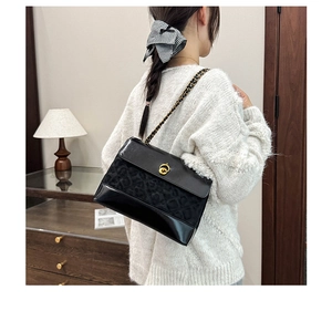 Detail of black quilted chain bag with gold rotary clasp on a shoulder-carried model