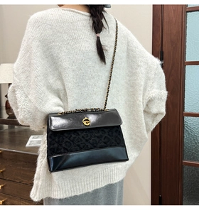 Detail of black quilted crossbody bag with golden twist lock and metal chain strap