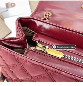 Detail view of smooth golden metal zipper and burgundy quilted leather texture on handbag