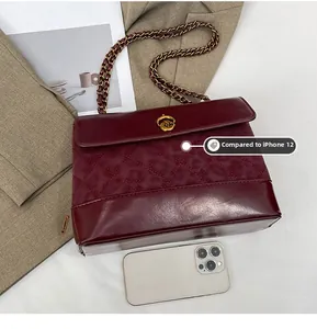 Detail view of deep red quilted chain bag with gold rotary lock beside a phone