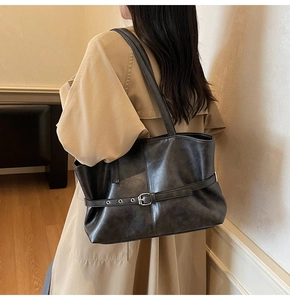 Detail showing the dark grey faux leather texture and metallic buckle strap on a tote bag