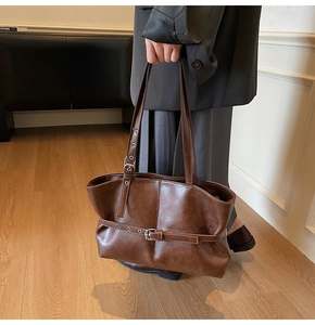 Close-up of a dark brown leather tote bag with stylish buckle strap and metal eyelet details