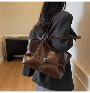 Detailed side view of deep brown tote bag with metal buckle strap and textured leather