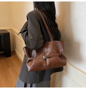 Close-up of deep brown vintage tote bag with decorative eyelet strap on model's shoulder