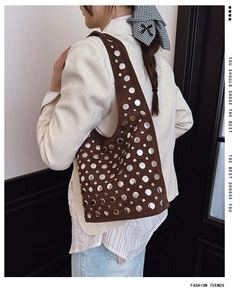 Borsa a spalla scamosciata marrone scuro con borchie argentate su un blazer bianco
