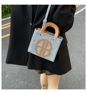 Detail of grey felt tote bag featuring brown leather letter patch and crossbody strap
